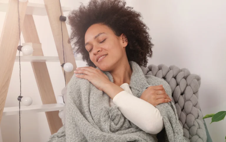 Woman practicing self-compassion, wrapped in a blanket, symbolizing mindfulness and emotional wellbeing.