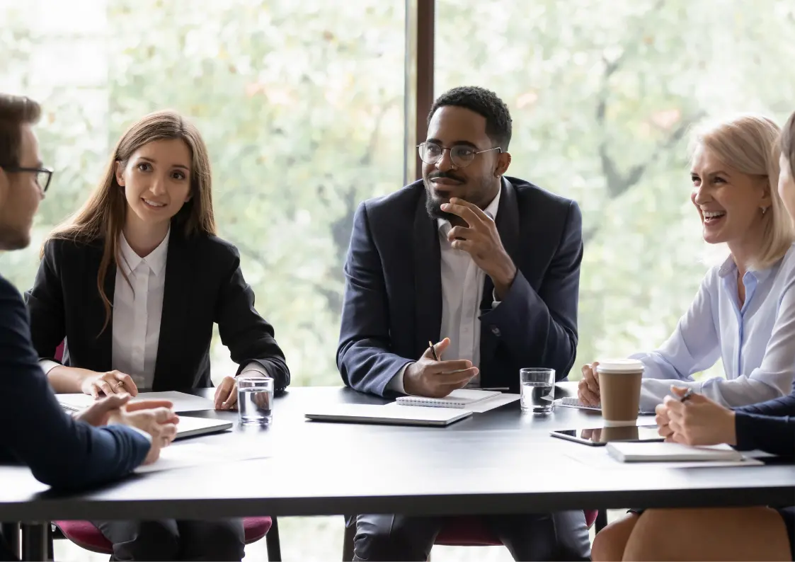 leadership A diverse group of professionals engaged in a calm, thoughtful discussion around a meeting table, reflecting mindful and emotionally intelligent leadership in a bright, natural-light office setting.