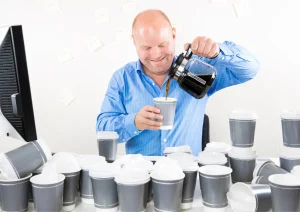 Man pouring coffee into a cup surrounded by multiple takeaway cups, illustrating habitual behaviour and overconsumption