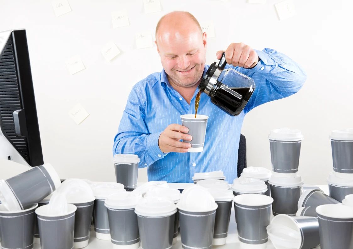 Man pouring coffee into a cup surrounded by multiple takeaway cups, illustrating habitual behaviour and overconsumption